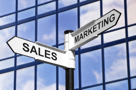 Concept image of Sales & Marketing on a signpost against a modern glass office building.